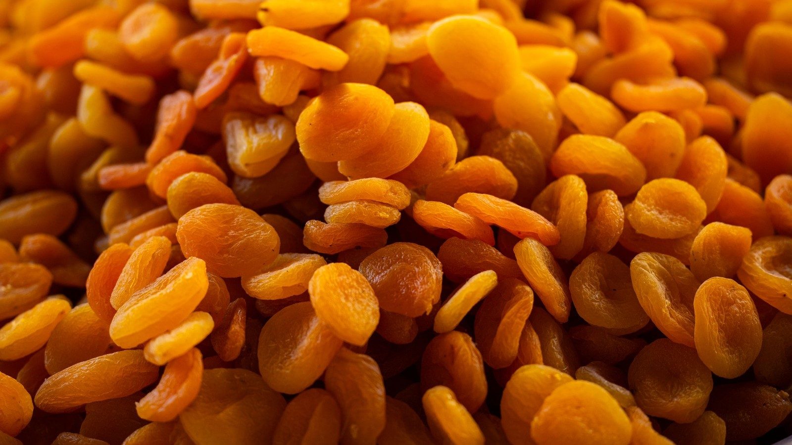 Monte de damascos secos inteiros, cor âmbar natural, textura enrugada, usados como matéria-prima em confeitaria e food service