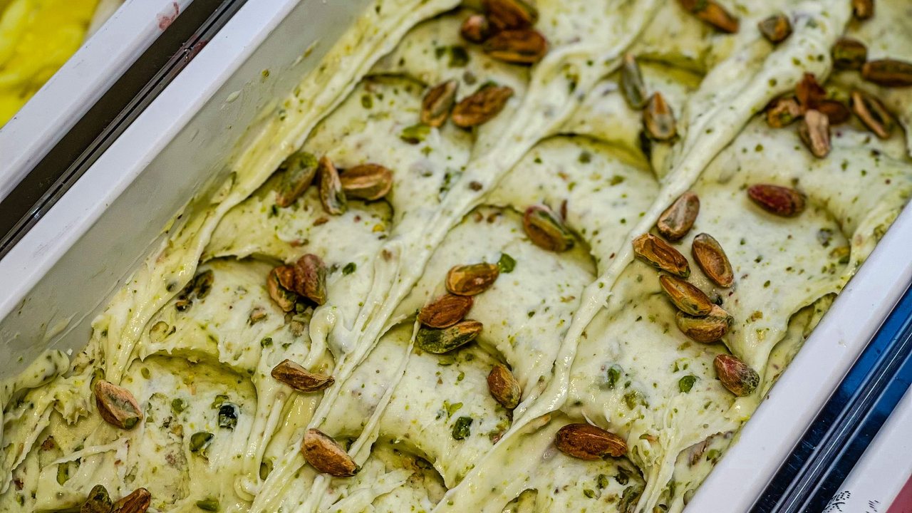 Gelato artesanal de pistache em cuba profissional de aço inox, com dobras de espátula e fragmentos de pistache